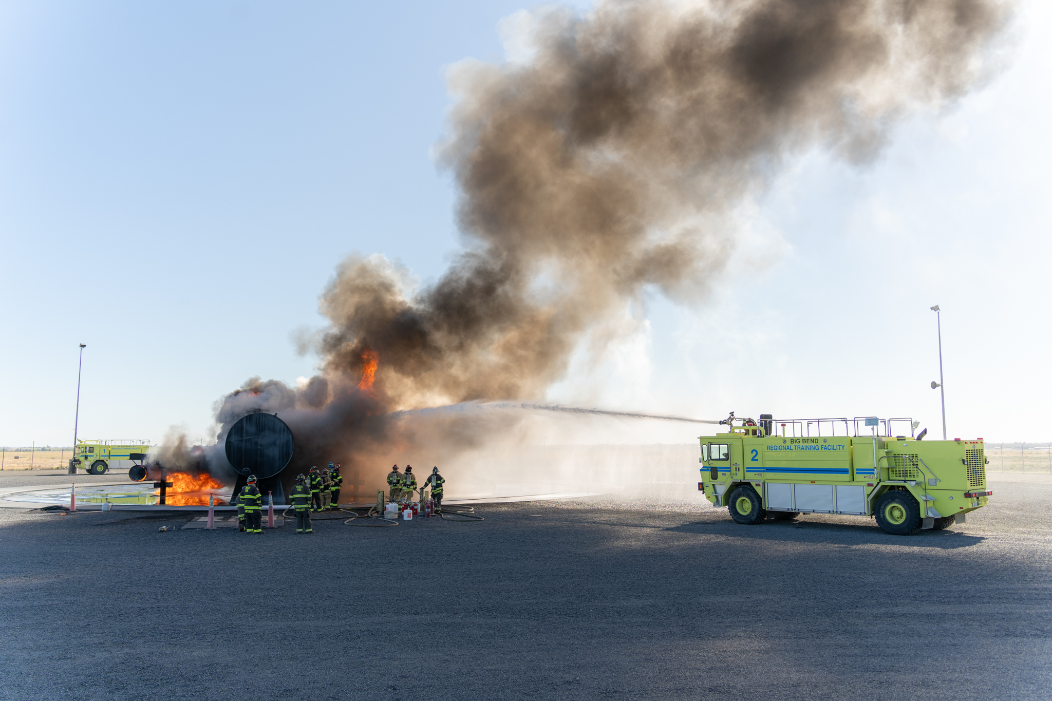 Yellow tanker truck sprays water on burning plane