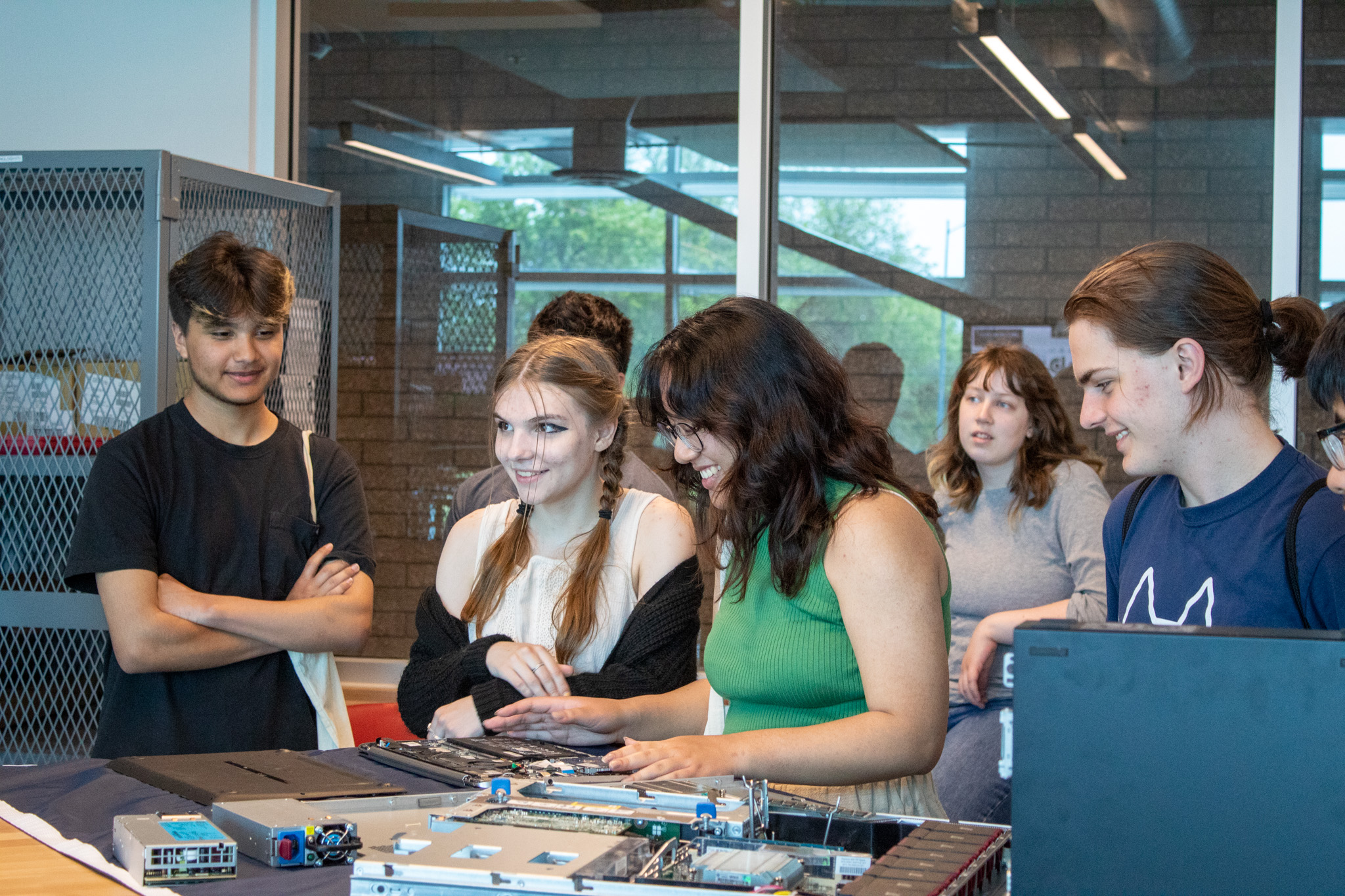 Several students look at and touch a disassembled computer on a table.